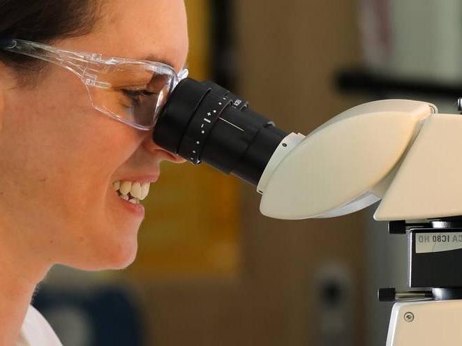 Woman is wearing safety goggles looking into a biology microscope