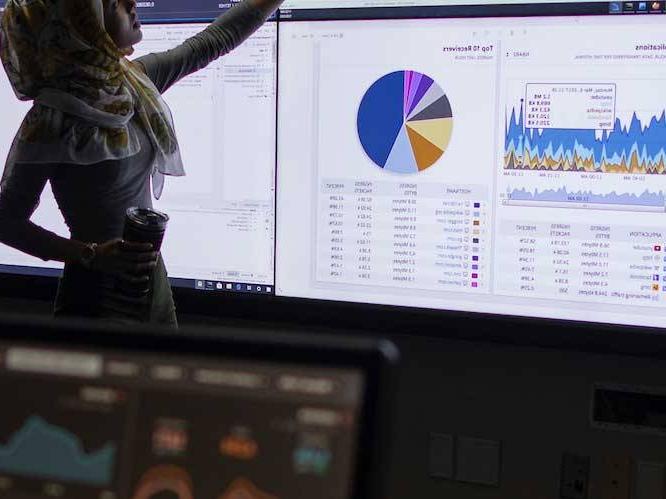 Woman standing infront of projector pointing to colorful graphs on screen